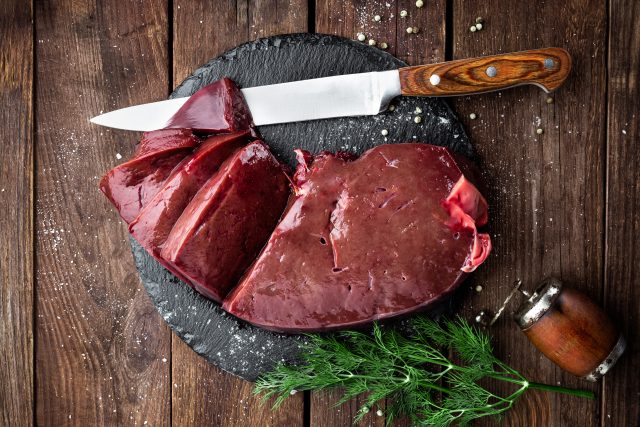 Raw liver on slate board on wooden background top view